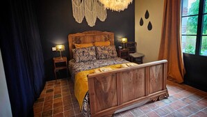 A bedroom with a wooden bed, macramé wall hanging, and a hanging light fixture. - Chambre de Charme, Gîte de L'archerie (Saint-Lambert-la-Potherie)
