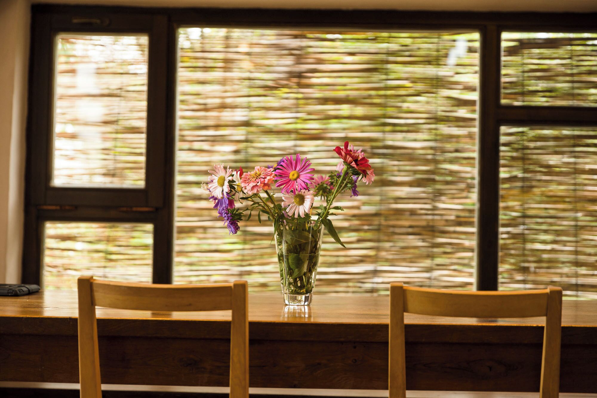 Ein Holztisch mit einer klaren Glasvase und bunten Blumen.