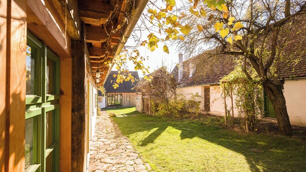 A stone pathway leading to a wooden building with a green door. - Viscri 125 (Bunesti)