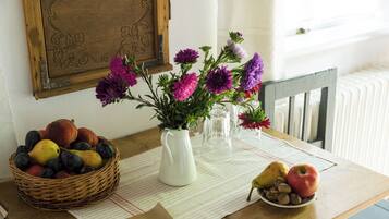 A table with a wicker basket of fruits, a vase with flowers, and a plate with nuts and a pear.