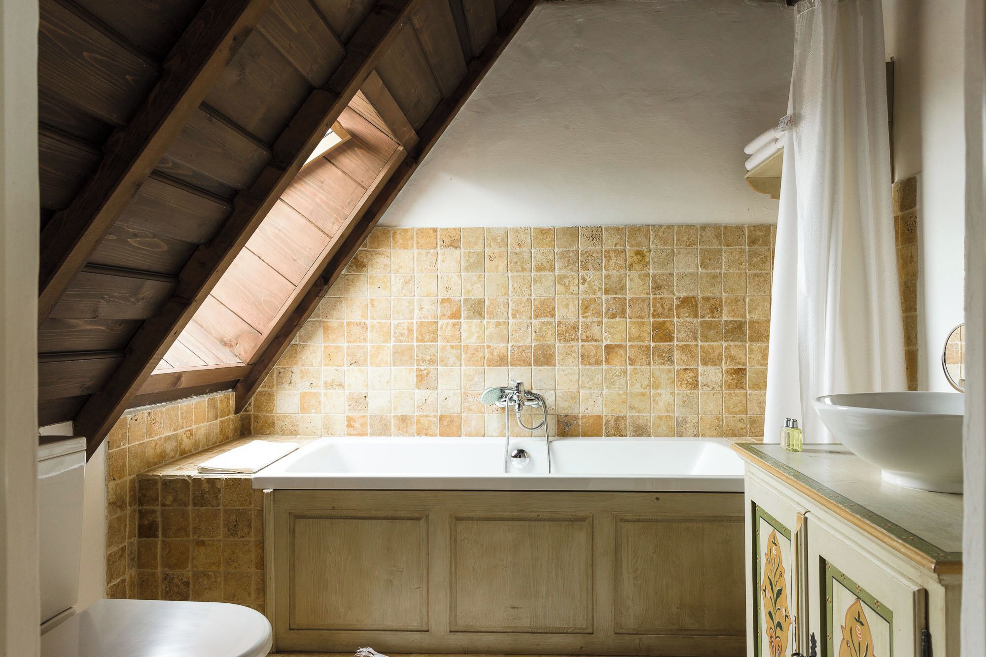 Ein Badezimmer mit schrägverdeckelter Decke, einer Badewanne, einer Dusche und einem WC.