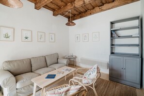 Una sala de estar acogedora con un sofá, una mesa de centro, un sillón de mimbre, una estantería e impresiones botánicas enmarcadas en la pared.