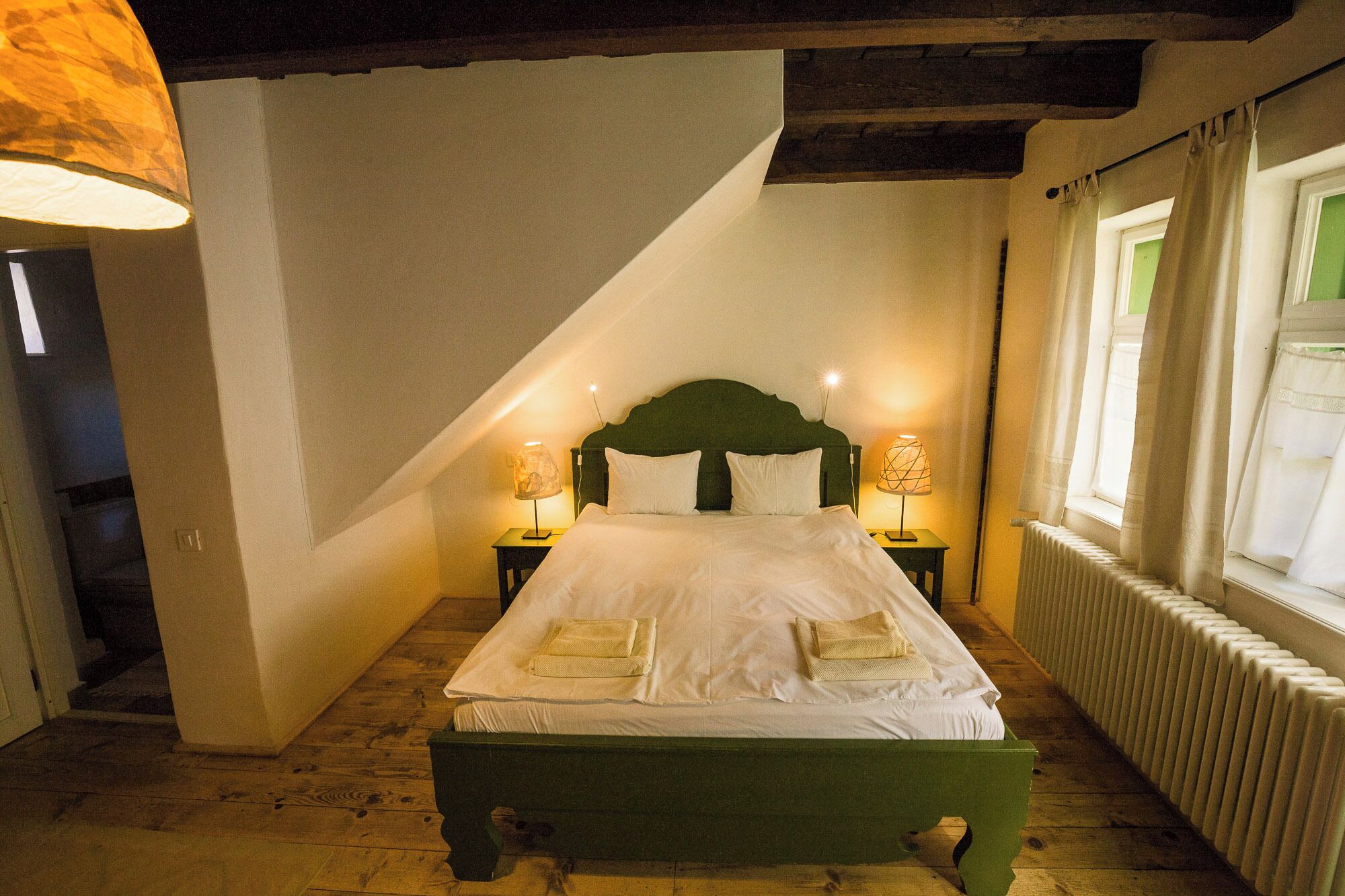 Una camera da letto con soffitto spiovente, una cornice del letto verde, due lampade ai comodini e un termosifone.