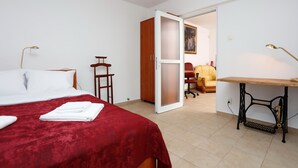 A bedroom with a bed, a red bedspread, a wooden wardrobe, a sewing machine, and a chair. - Premium one-bedroom suite in the heart of Bucharest  (București)