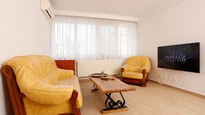 A living room with a yellow sofa, a wooden coffee table, and a television on the wall. - Premium one-bedroom suite in the heart of Bucharest  (București)