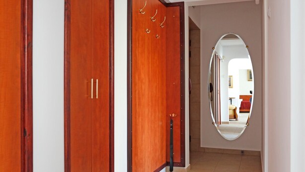A hallway with wooden doors, a tiled floor, and a mirror reflecting a room with a red sofa. - Premium one-bedroom suite in the heart of Bucharest  (București)