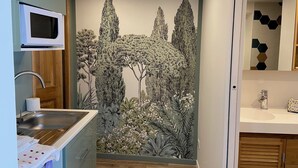A kitchen with a microwave, sink, and wooden cabinets. There is a wall mural of trees and foliage. - Studio in Seguret. Lisanathis (Seguret)
