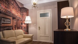 Een kamer met een beige leren bank, een houten kast, een witte deur en een kroonluchter.