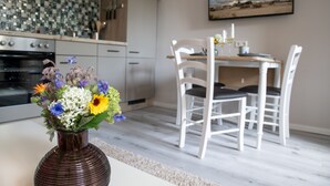 Een moderne keuken met een betegelde spatwand, een eethoek met witte stoelen en een vaas bloemen op het aanrecht.