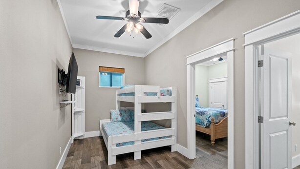 Una cuccetta per bambini con una ventola a soffitto, un pavimento in legno e una porta che conduce in un'altra stanza.