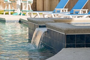 Ein Pool mit Wasserfall und Liegestühlen im Hintergrund.