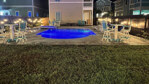 Area piscina residenziale con lettini e una piccola vasca, circondata da una recinzione in legno e luci decorative.