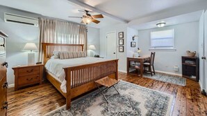 A bedroom with a wooden bed, a desk, a chair, a ceiling fan, and a window with blinds.