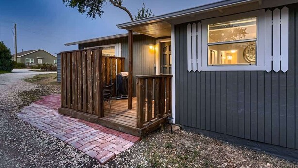 A small, single-story building with a wooden deck and a brick pathway leading to the entrance.