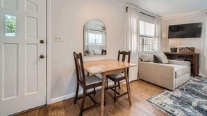 A dining area with a wooden table and chairs, a sofa, a TV, and a window with curtains.