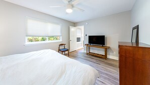 Quarto com cama, televisão, ventilador de teto, janela com persianas e porta.