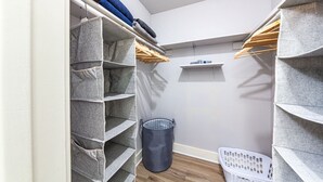 Um closet espaçoso com caixas organizadoras cinzas, cabides de madeira e um cesto de roupa cinza.