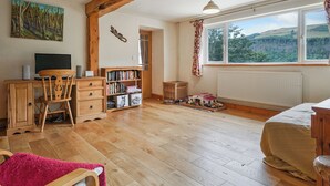 A cozy room with wooden floors, a desk with a computer and speakers, a bookshelf, a window with a view of the countryside, and a bed with a red blanket. - Delfryn, Goginan (Aberystwyth)