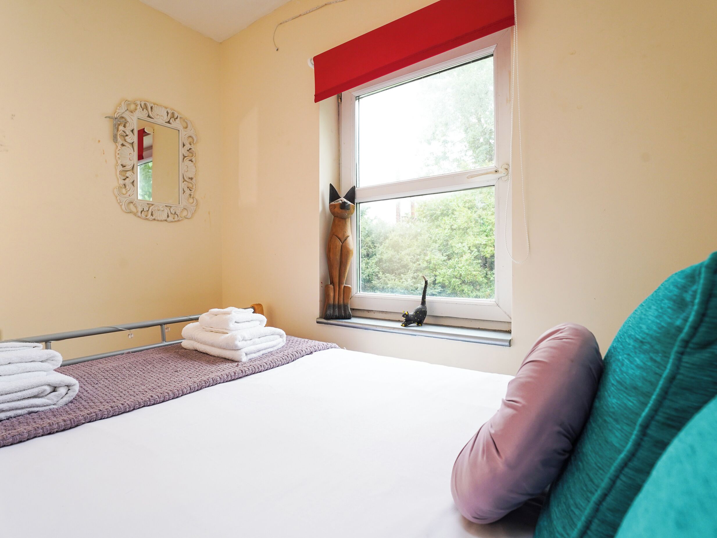 A bedroom with a bed, a window with a view of trees, a mirror, and a towel rack.