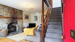 A cozy living room with a stone wall, a fireplace, a sofa with a yellow blanket, a television, and a staircase. - Delfryn, Goginan (Aberystwyth)
