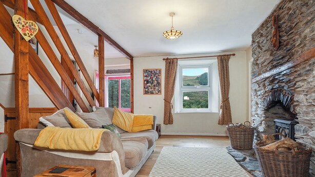 A cozy living room with a wooden staircase, a fireplace, and a large window with curtains. - Delfryn, Goginan (Aberystwyth)
