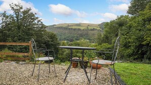An outdoor seating area with a table and chairs, gravel ground, and a scenic view of hills and trees. - Delfryn, Goginan (Aberystwyth)