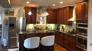 A modern kitchen with wooden cabinets, stainless steel appliances, and a central island with bar stools. - ROUND HOUSE SANDUSKY. Heated inground pool, your own oasis! (Sandusky)