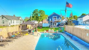 A backyard with a swimming pool, lounge chairs, and a covered patio area. - ROUND HOUSE SANDUSKY. Heated inground pool, your own oasis! (Sandusky)