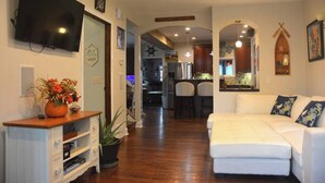 A living room with a white sofa, a TV mounted on the wall, and a wooden cabinet with a vase of flowers. - ROUND HOUSE SANDUSKY. Heated inground pool, your own oasis! (Sandusky)