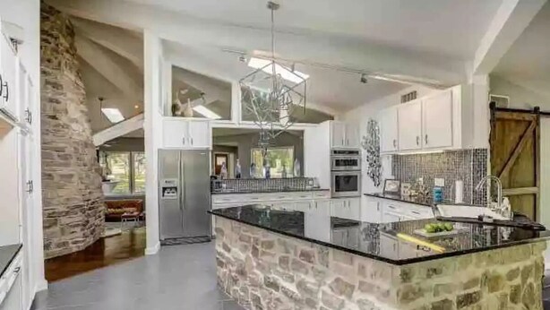 A spacious kitchen with a large island, stone accents, and modern appliances. - Your OASIS Nestled In Wooded River Views, POOL (Manchaca)