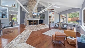 A spacious living area with a stone fireplace, modern furniture, and large windows offering views of the outdoors. - Your OASIS Nestled In Wooded River Views, POOL (Manchaca)