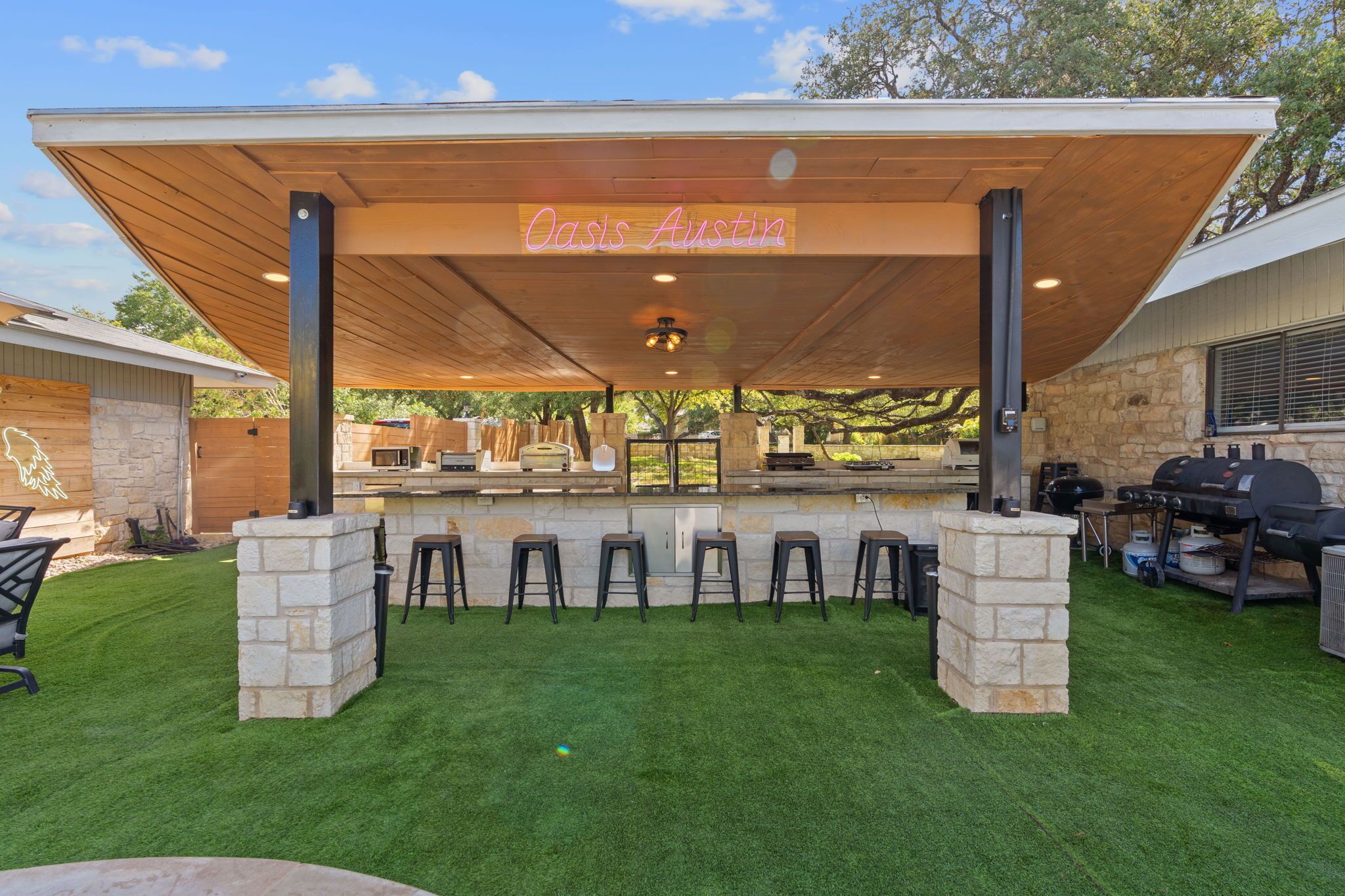 Un área de bar al aire libre con un toldo de madera, pilares de piedra y una estación de parrilla.