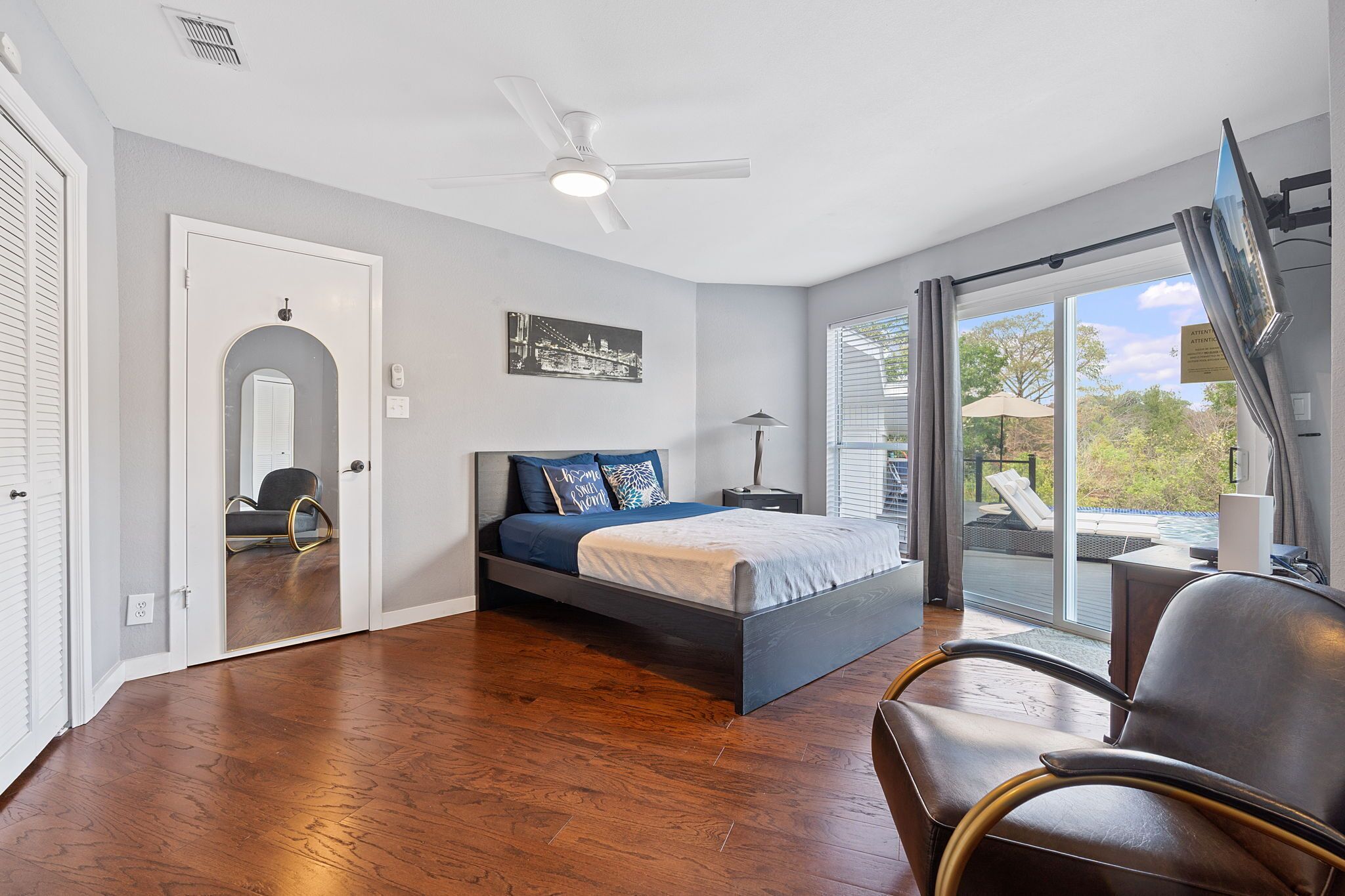 A bedroom with a bed, a chair, a ceiling fan, and a view of the outdoors.