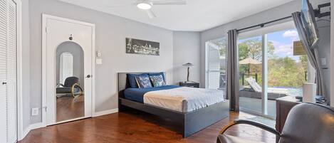 A bedroom with a bed, a chair, a ceiling fan, and a view of the outdoors.