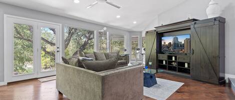 A spacious living room with a grey sofa, a ceiling fan, and a television on a wooden cabinet.