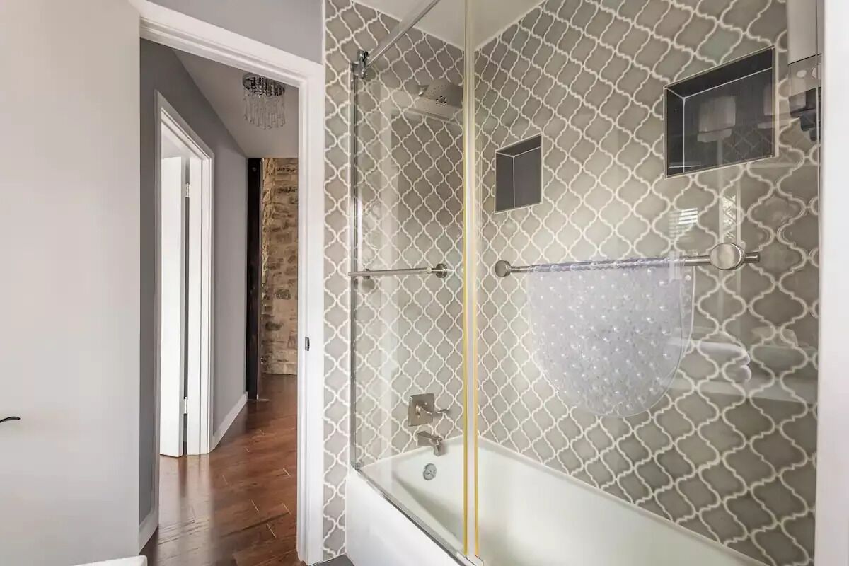 Ein Badezimmer mit einer Duschkabine, einer Badewanne und einer gefliesten Wand mit geometrischem Muster.