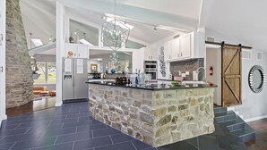 A spacious kitchen with a central island, stone accents, and modern appliances. - Your OASIS Nestled In Wooded River Views, POOL (Manchaca)