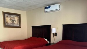 Habitación de hotel con dos camas, aire acondicionado instalado en el techo, un cuadro en la pared y una lámpara de noche.