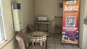 Un pequeño patio amurallado con una mesa y dos sillas, un microondas sobre una mesita, un cubo de basura y un gran cartel promocional.
