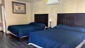 Habitación de hotel con dos camas, un cuadro en la pared, aire acondicionado y una mesita de noche con lámpara.