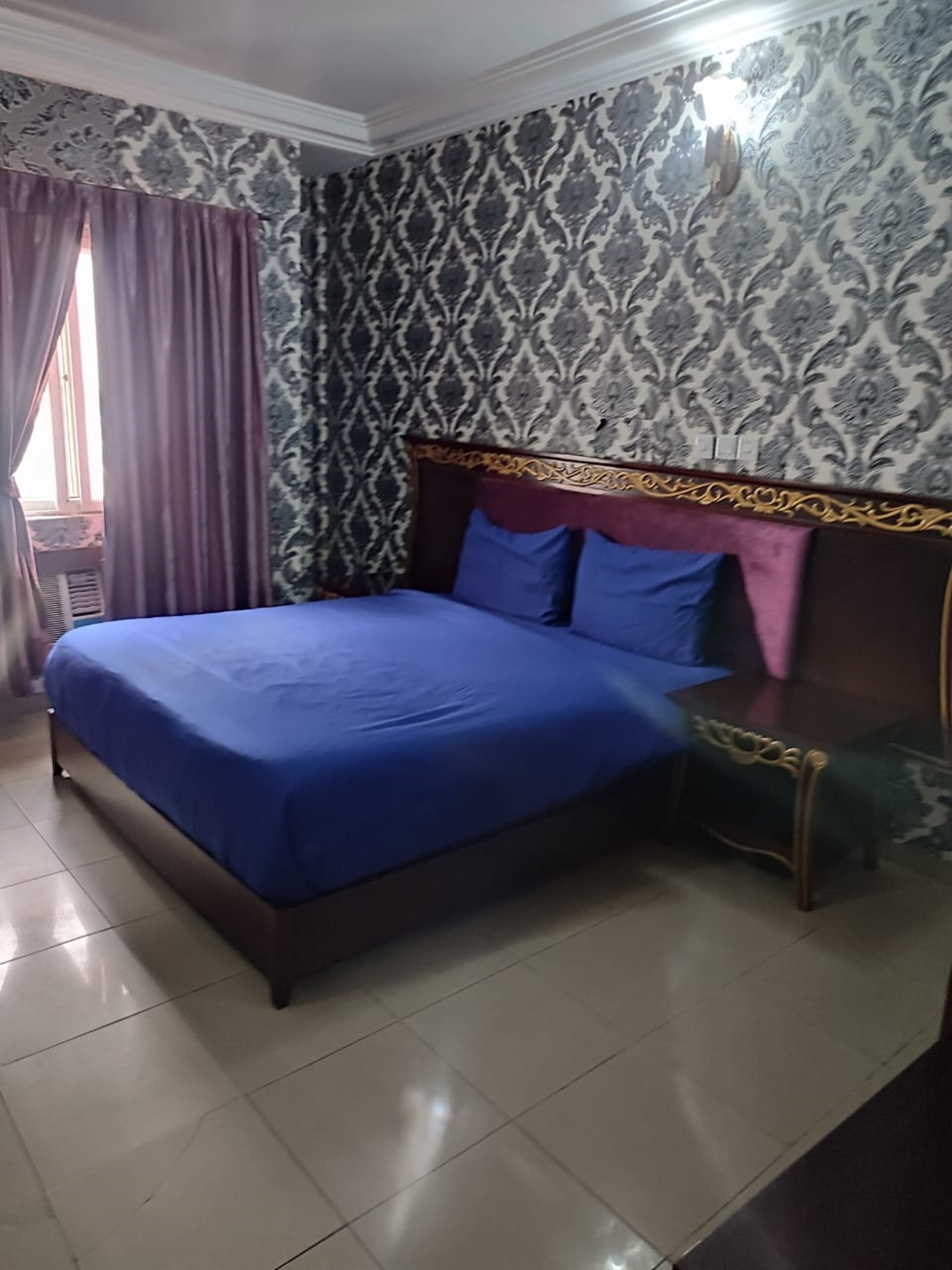 Quarto com cama, cortinas, papel de parede estampado e mesa de cabeceira.