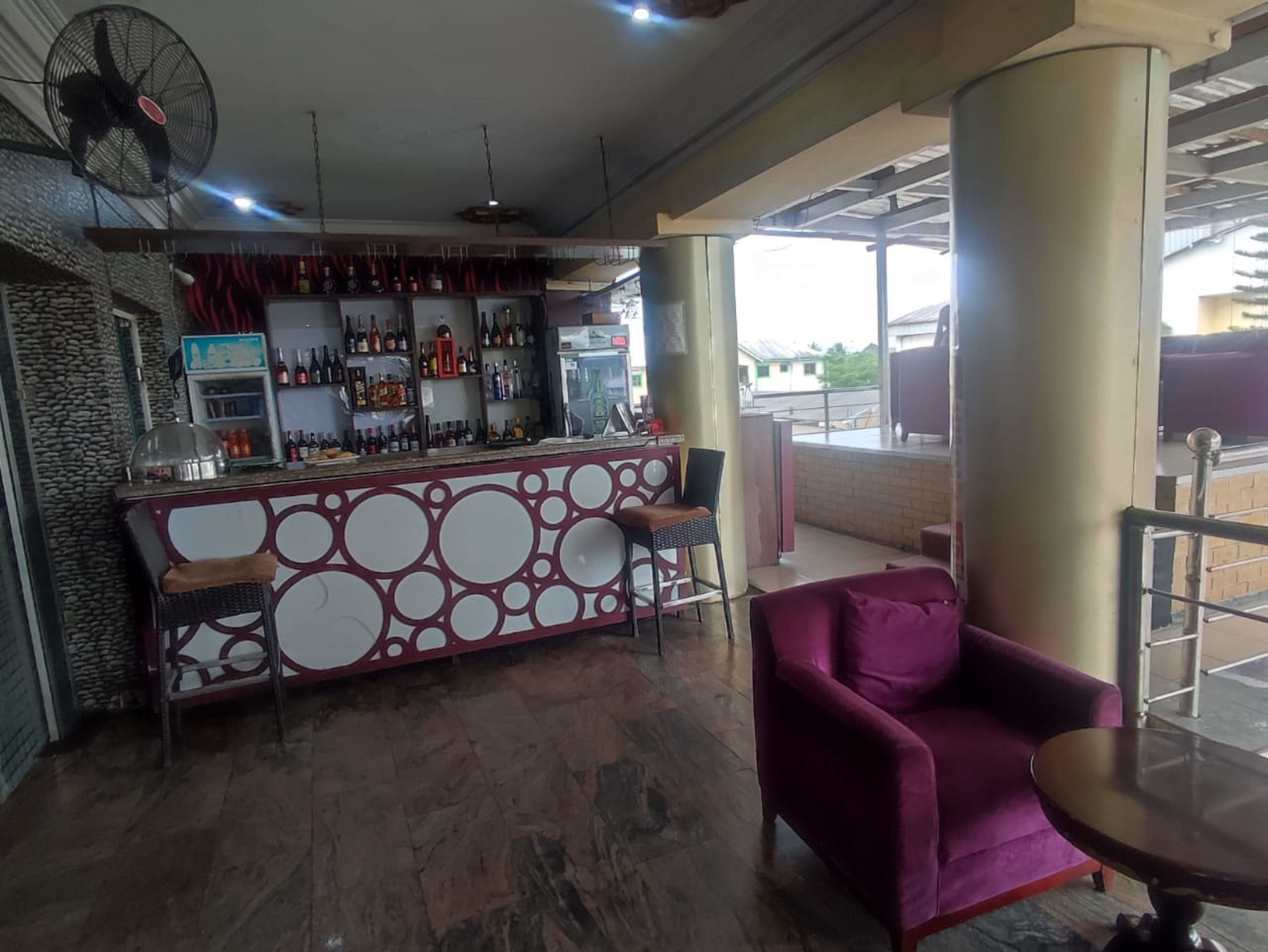 A bar area with a counter, shelves of bottles, a fan, and a purple chair.
