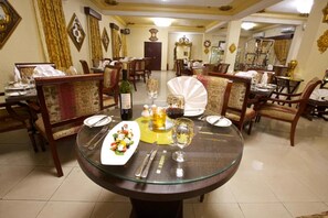 A dining area with round tables, chairs, and a variety of table settings including plates, cutlery, and glassware.