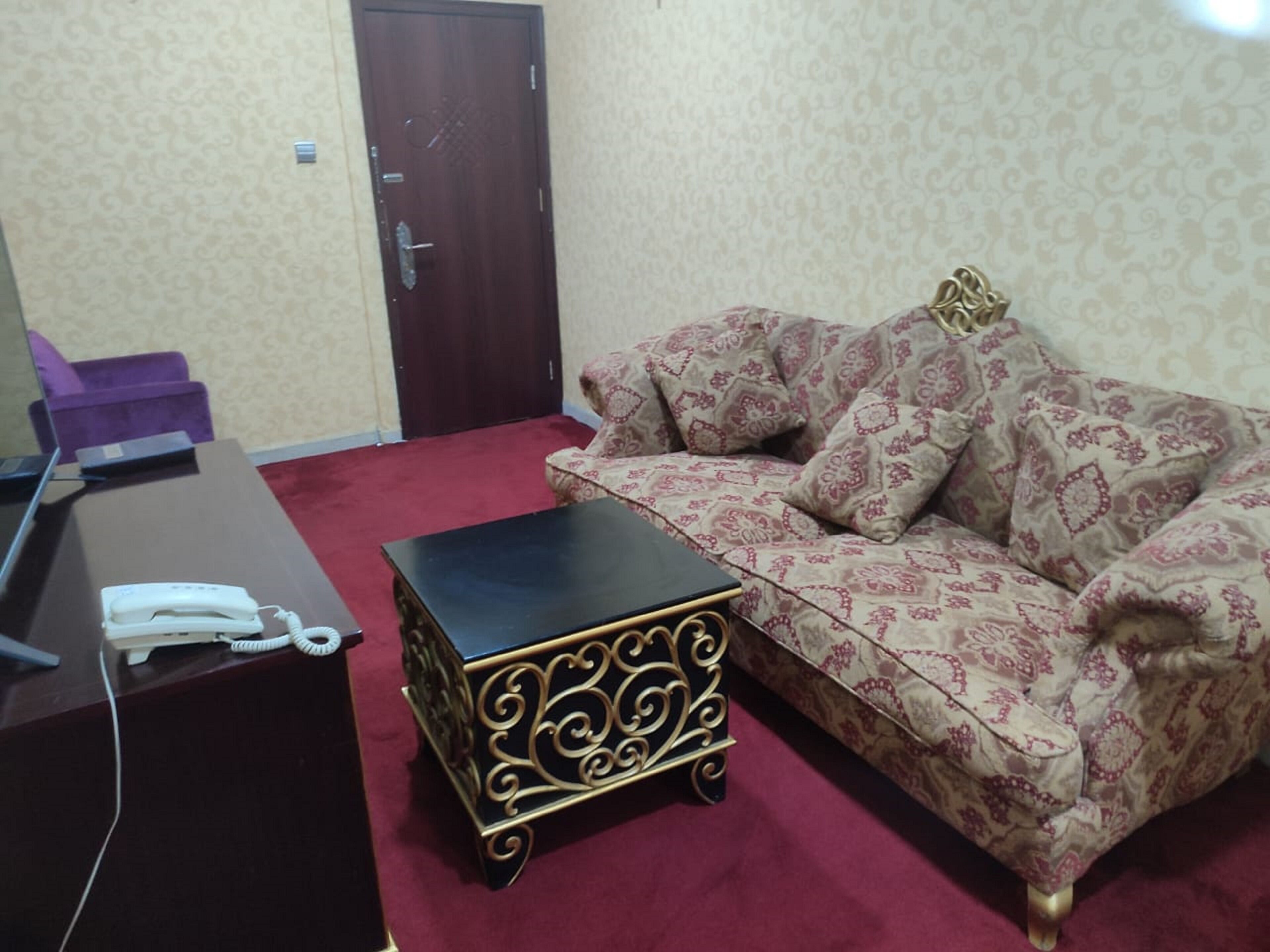 Ein Zimmer mit einer gemusterten Couch, einem kleinen schwarzen Beistelltisch mit Goldakzenten und einem Schreibtisch mit Telefon.