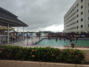 A swimming pool area with multiple pools, a covered seating area, and a building in the background.