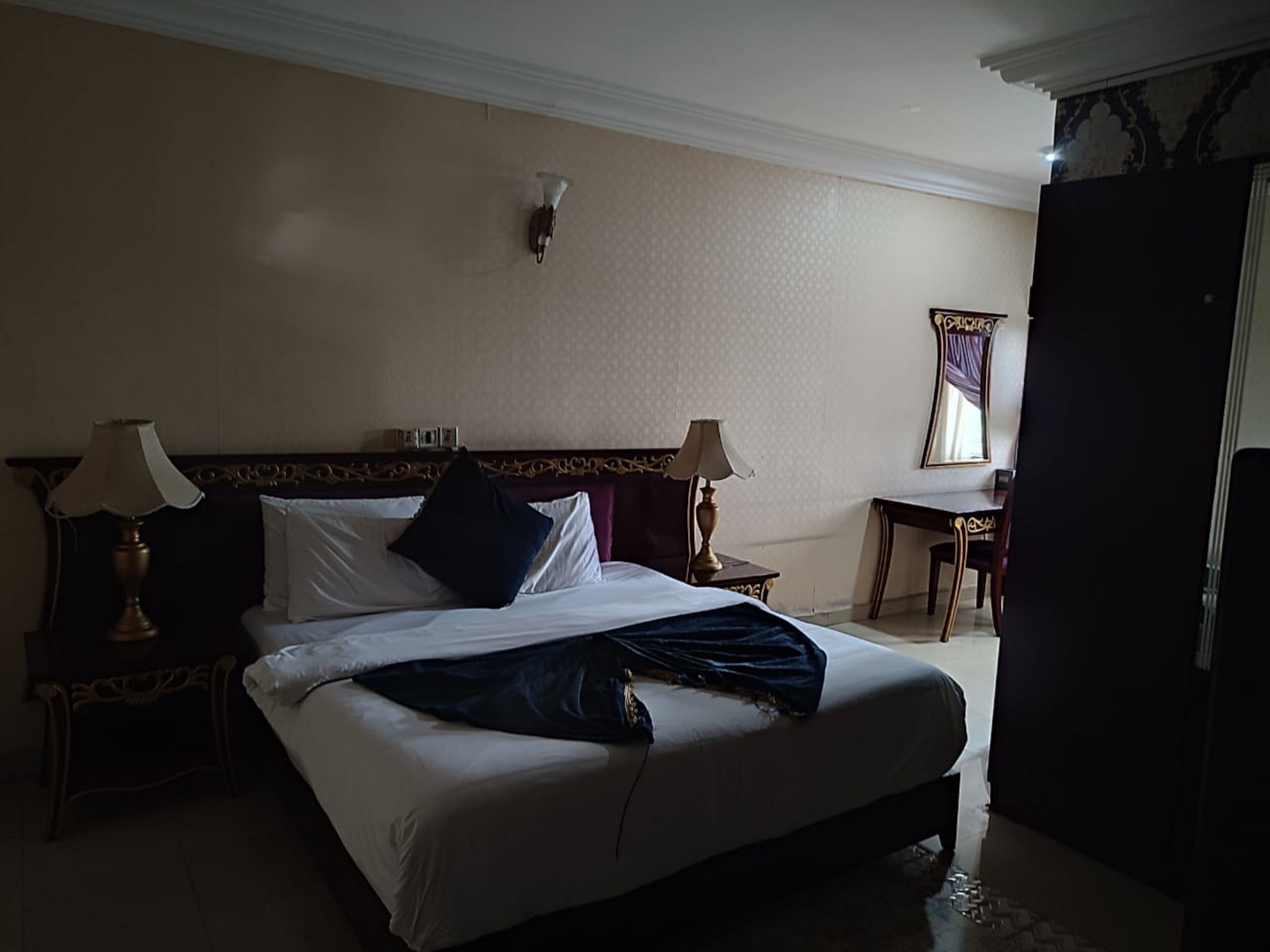 Ein Hotelzimmer mit einem großen Bett, zwei Nachttischen mit Lampen, einem Schreibtisch und einem Stuhl.