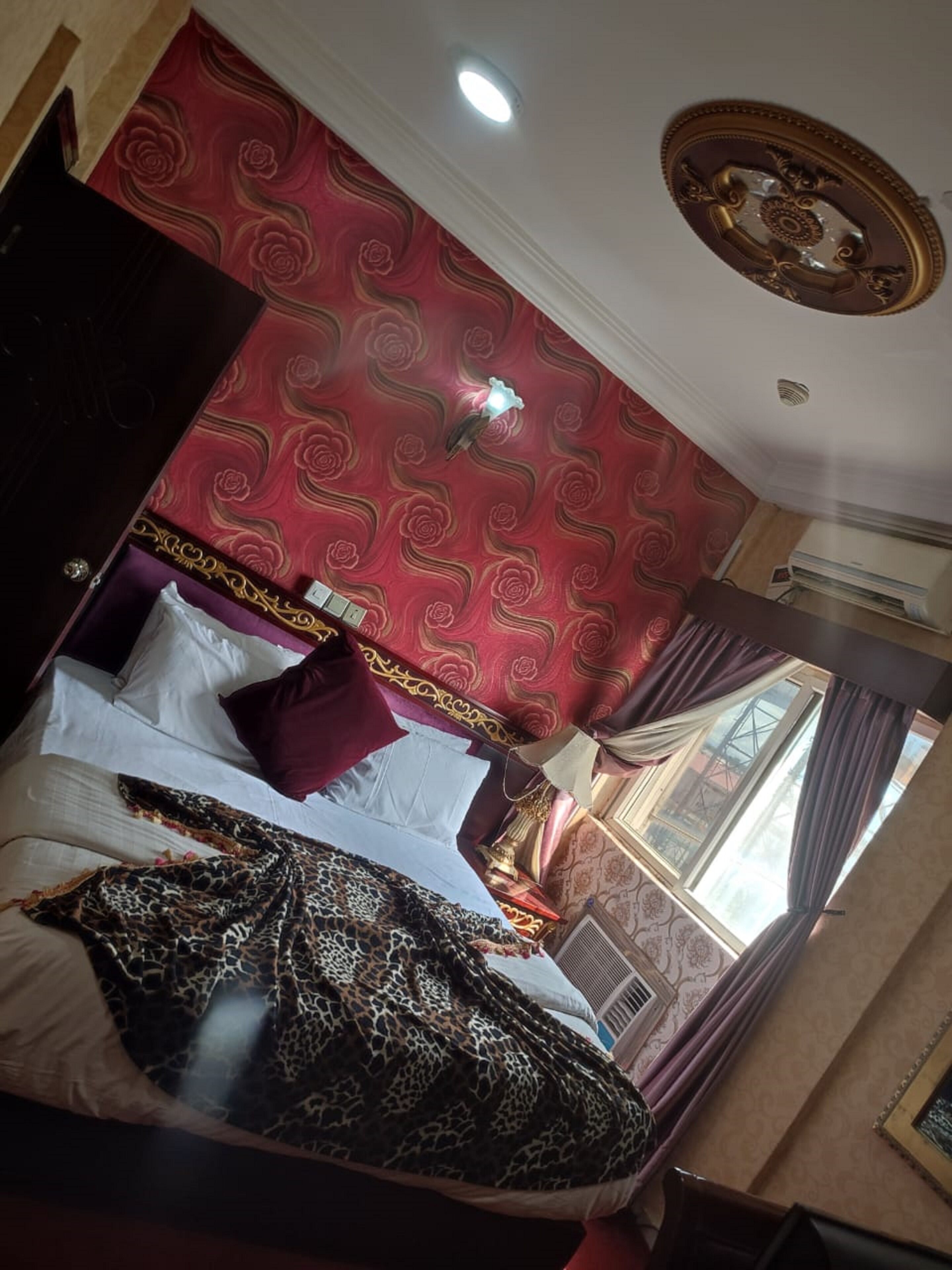 A hotel room with a red patterned wallpaper, a bed with a leopard print blanket, and a window with curtains.