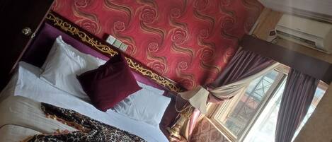A hotel room with a red patterned wallpaper, a bed with a leopard print blanket, and a window with curtains.
