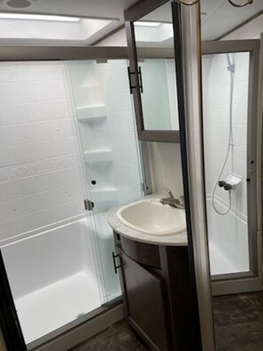 A bathroom with a glass shower enclosure, a white sink, and a mirror above it. - Current River Luxury in a Camper (Van Buren)