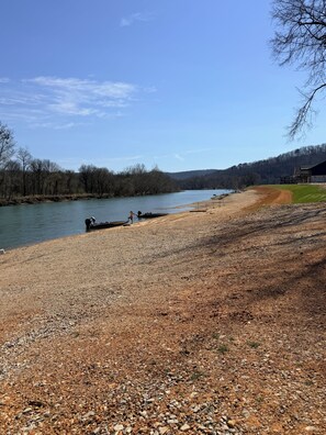 A gravel beach with a boat docked, a river, and a forested hillside in the background. - Current River Luxury in a Camper (Van Buren)
